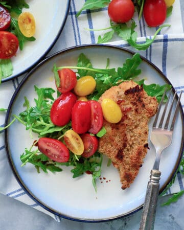 Top view of a plate filled with salad, tomatoes, and breaded chicken with tomatoes on the side.