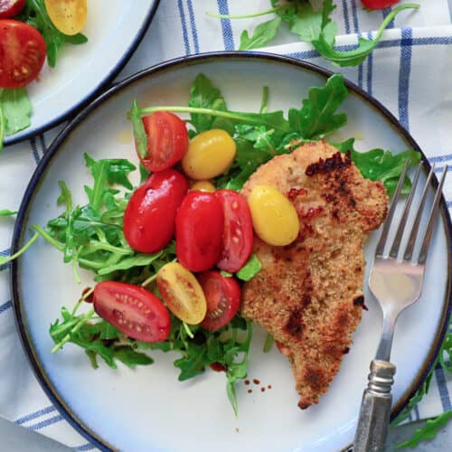 Top view of a plate filled with salad, tomatoes, and breaded chicken with tomatoes on the side.