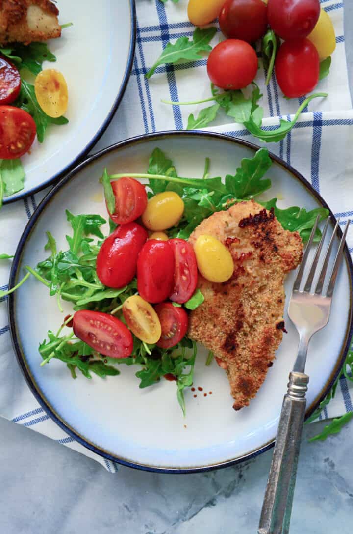 Top view of a plate filled with salad, tomatoes, and breaded chicken with tomatoes on the side.