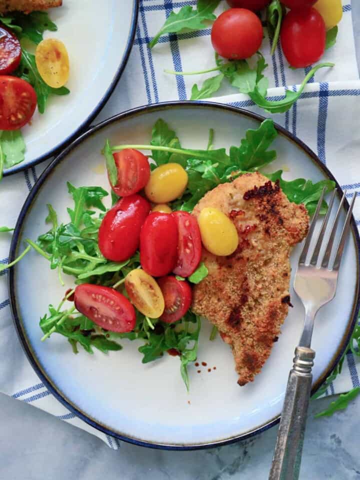 Top view of a plate filled with salad, tomatoes, and breaded chicken with tomatoes on the side.