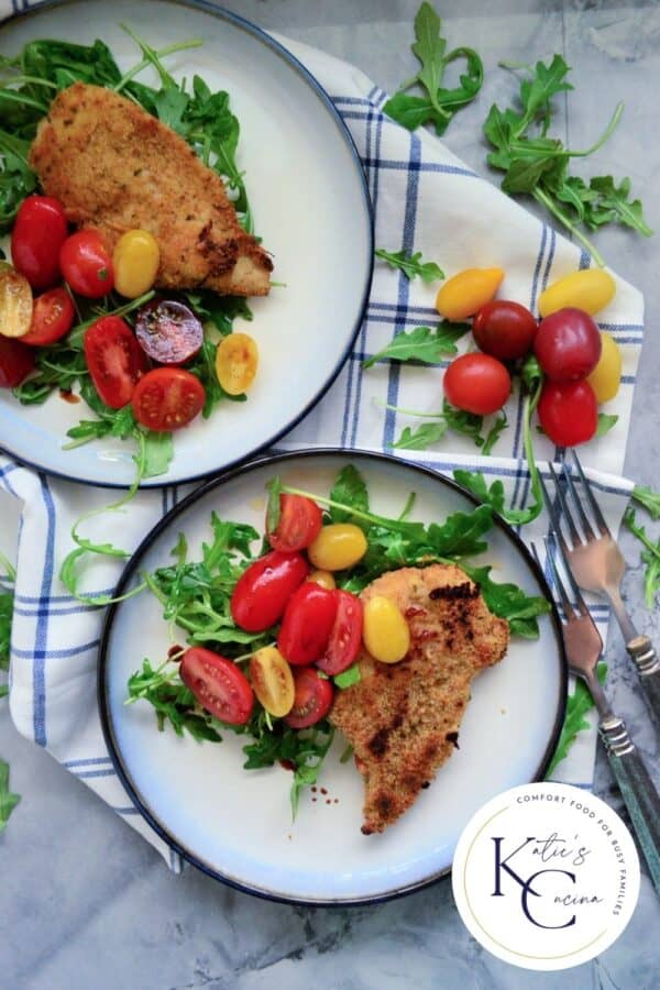 Top view of two white plates with salad, chicken breast and a logo on the right corner.