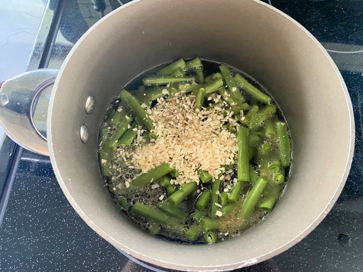 Top view of a brown pot with green beans, onions, and water.