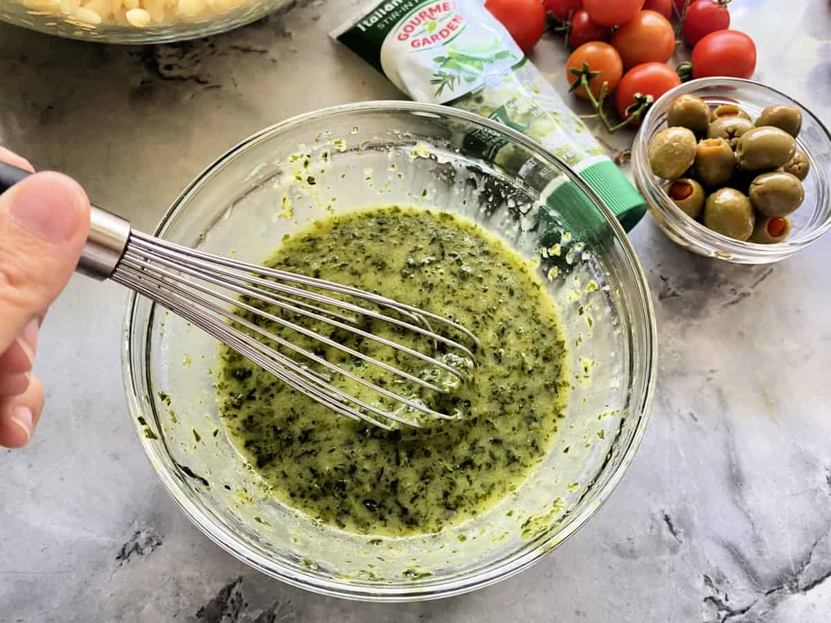 Top view of a female hand whisking an herb dressing together.