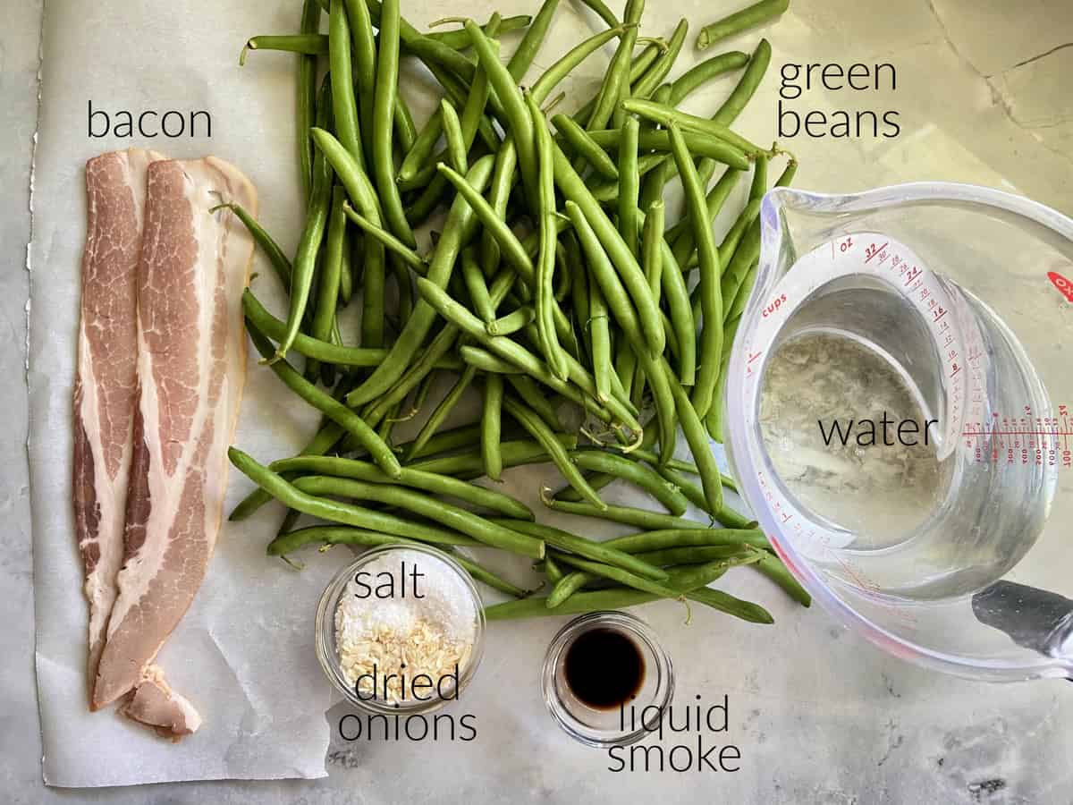 Ingredients on counter, bacon, green beans, salt, onions, liquid smoke, and water.