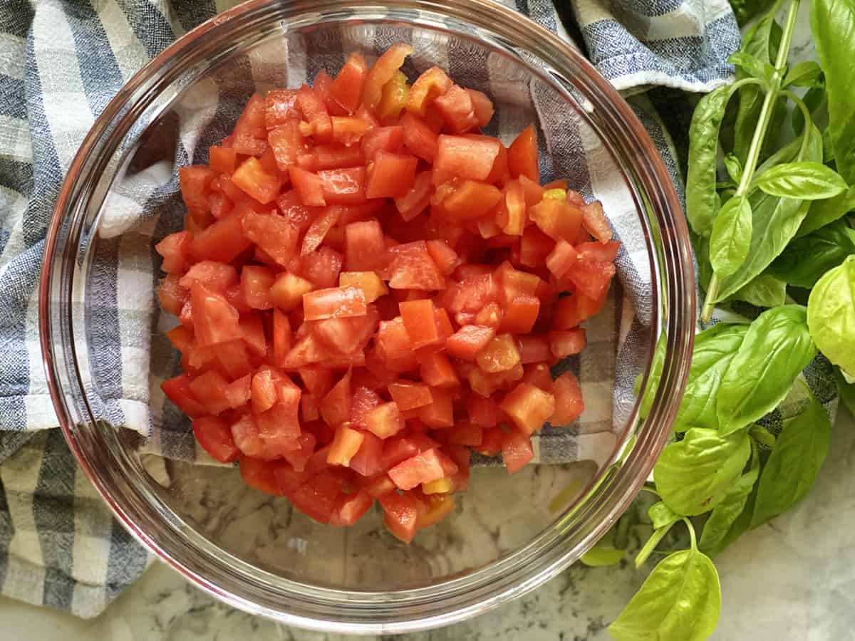 Top view of a glass bowl with diced tomatoes with basil on the side.