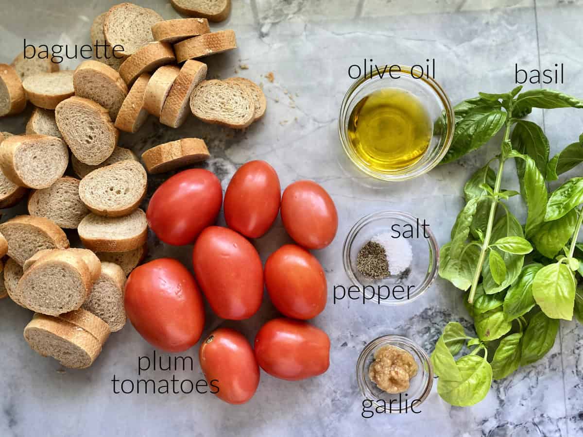 Ingredients on counter: baguette, plum tomatoes, olive oil, salt, pepper, basil, and garlic.