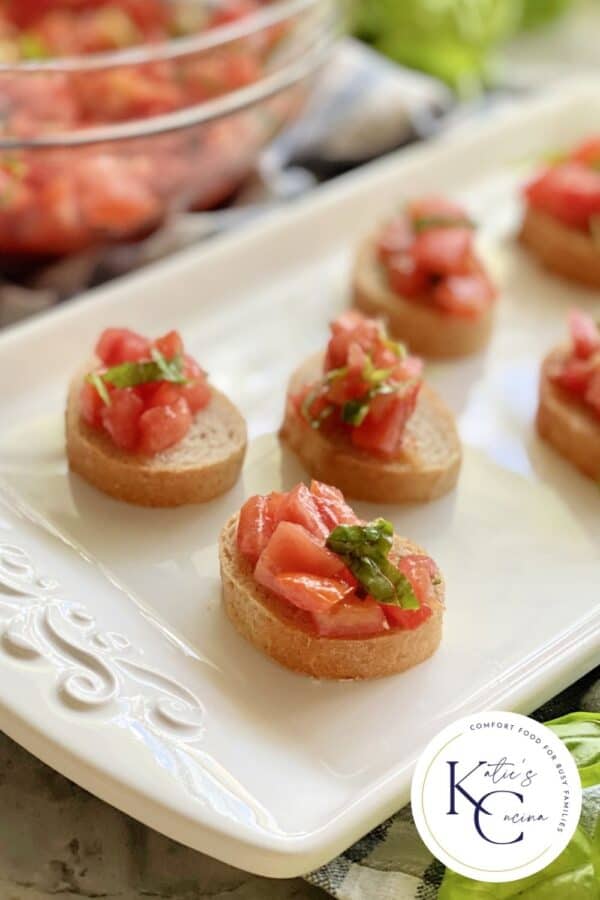 White platter filled with 6 pieces of bruschetta with logo on right corner.