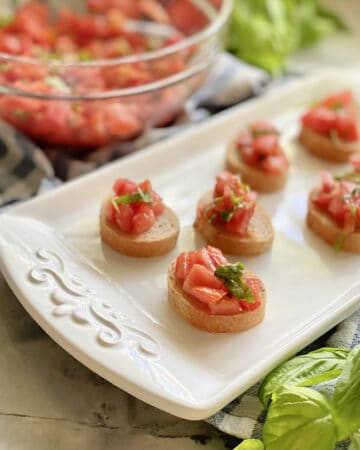 White platter with 6 pieces of baguettes with bruschetta on top.