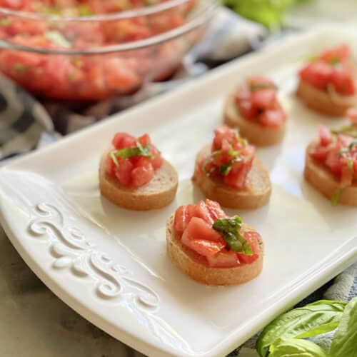 White platter with 6 pieces of baguettes with bruschetta on top.