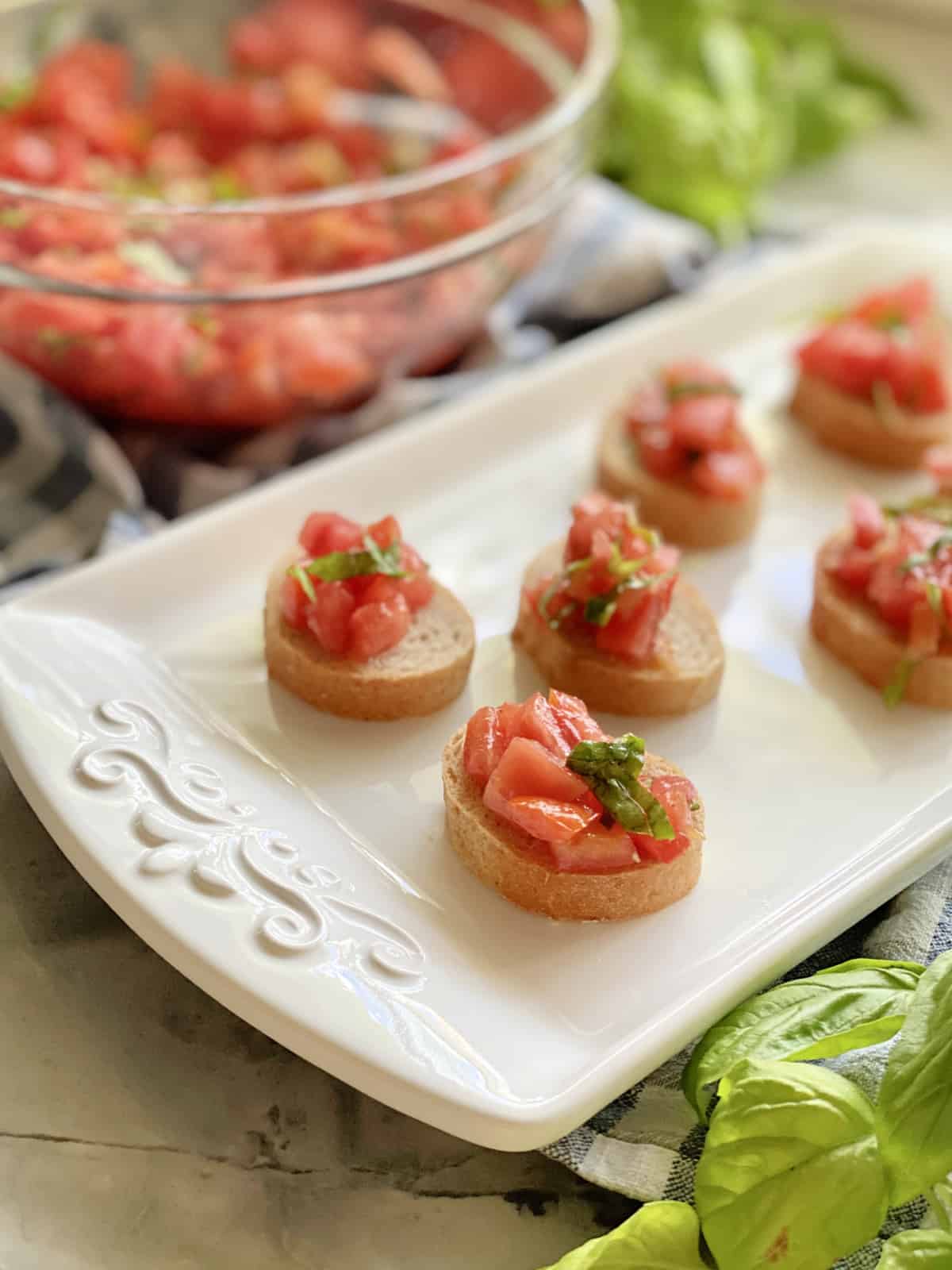 White platter with 6 pieces of baguettes with bruschetta on top.