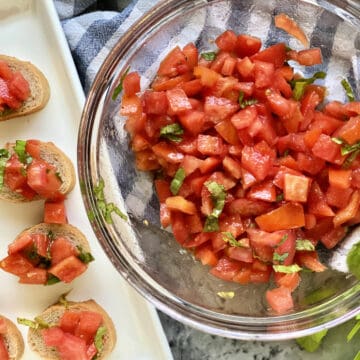 Top view of a glass bowl filled with diced tomatoes, basil, and a platter of bruschetta.