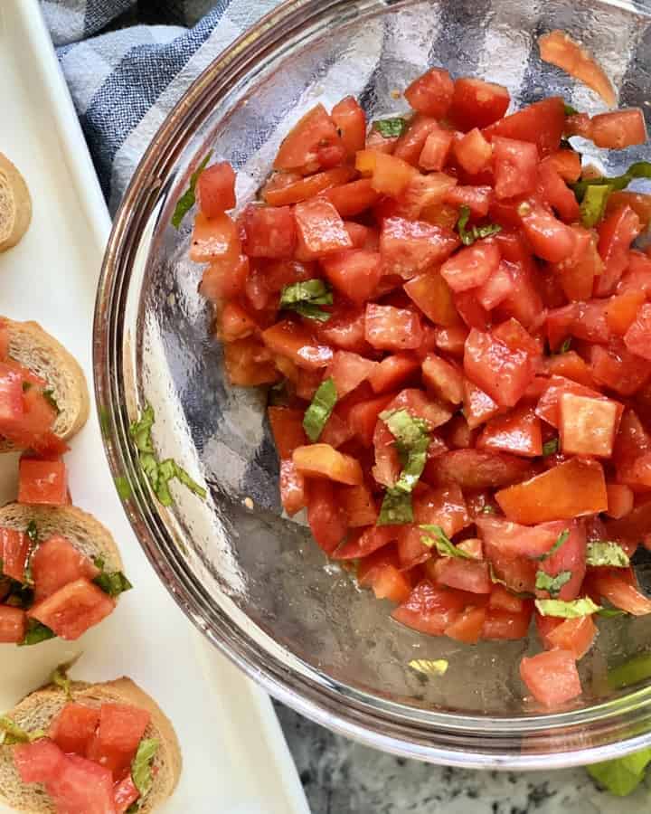 Top view of a glass bowl filled with diced tomatoes, basil, and a platter of bruschetta.