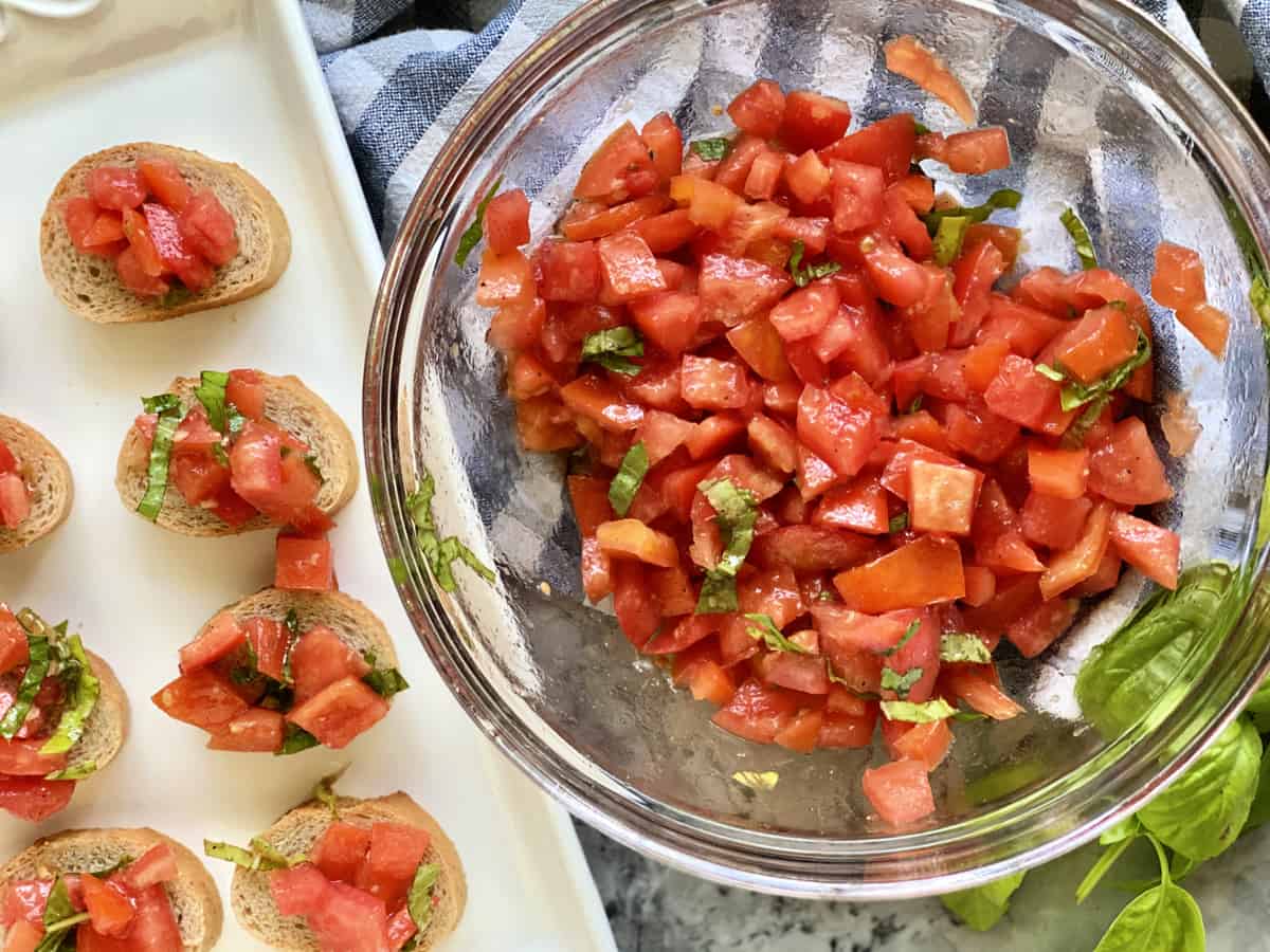 Top view of a glass bowl filled with diced tomatoes, basil, and a platter of bruschetta.