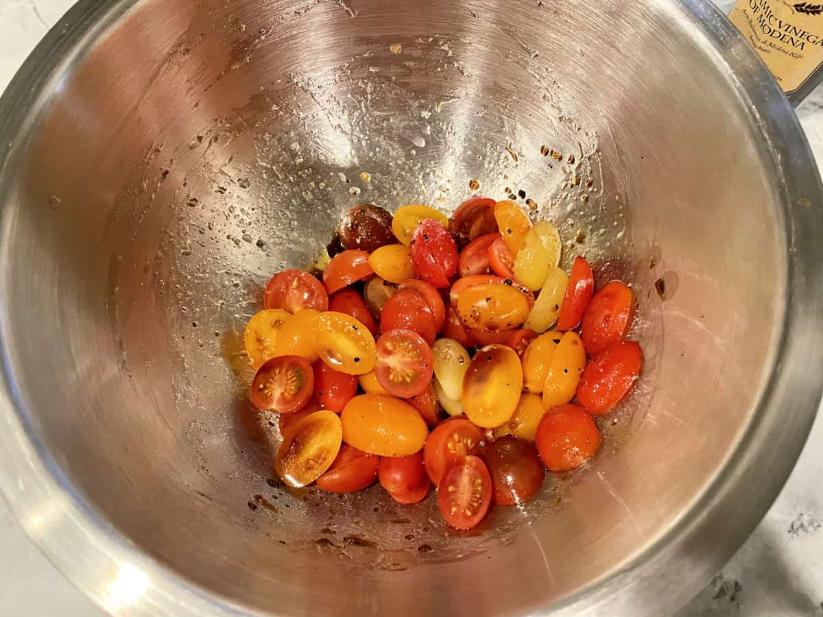 Top view of a silver bowl fileld with grape tomatoes cut in half and tossed in dressing.