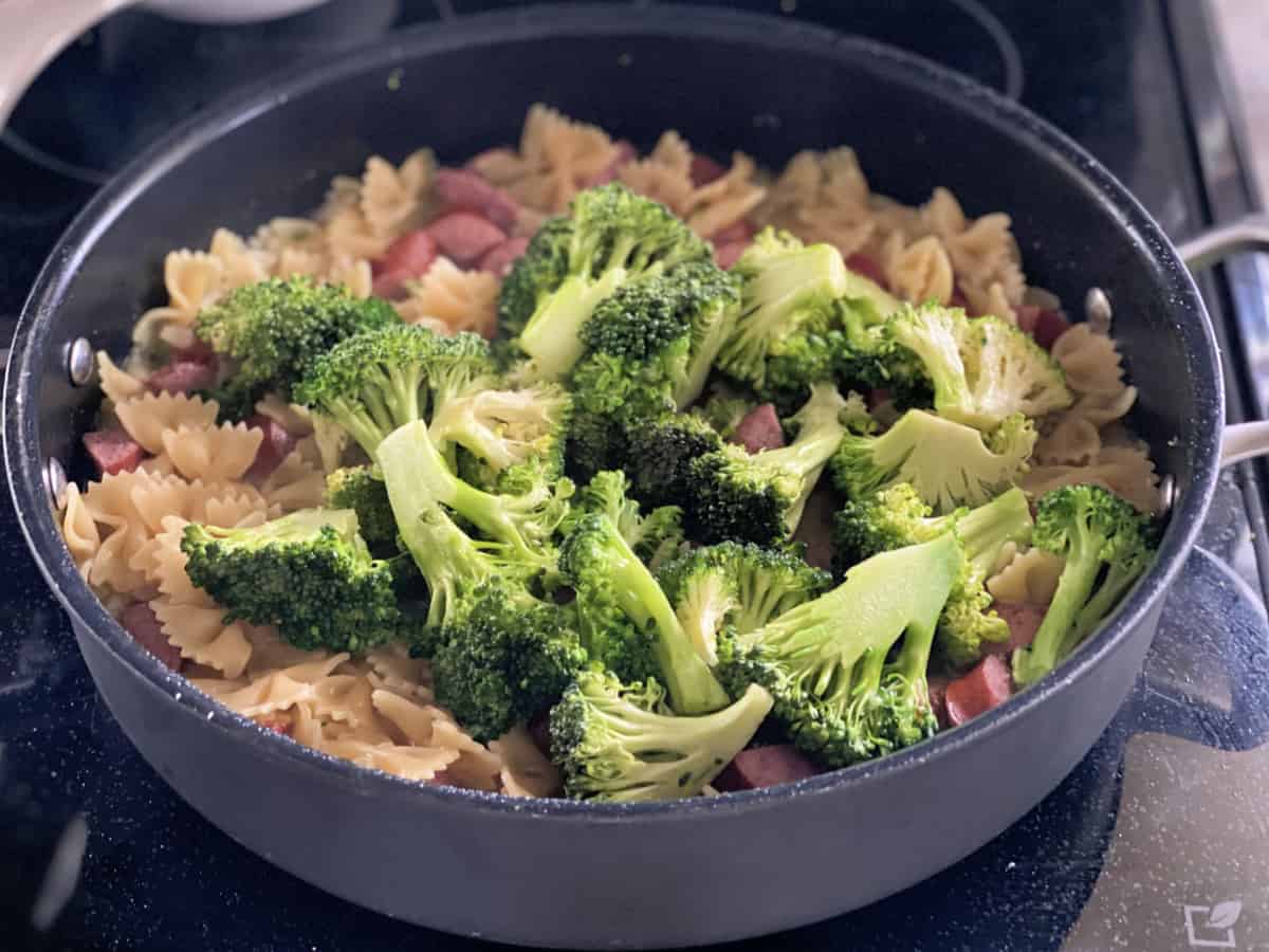 Black skillet filled with cooked pasta with broccoli on top.