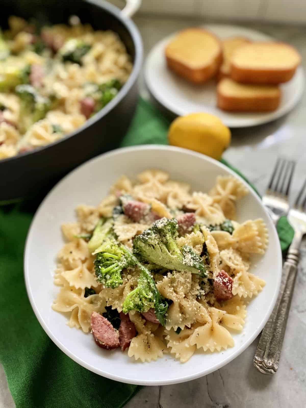 White shallow bowl filled with bow tie pasta, cheese, broccoli, and kielbasa.