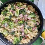 Top view of a black skillet filled with bow tie pasta, broccoli, kielbasa, and cheese.