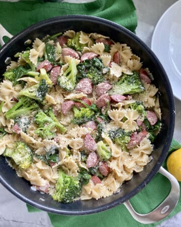 Top view of a black skillet filled with bow tie pasta, broccoli, kielbasa, and cheese.