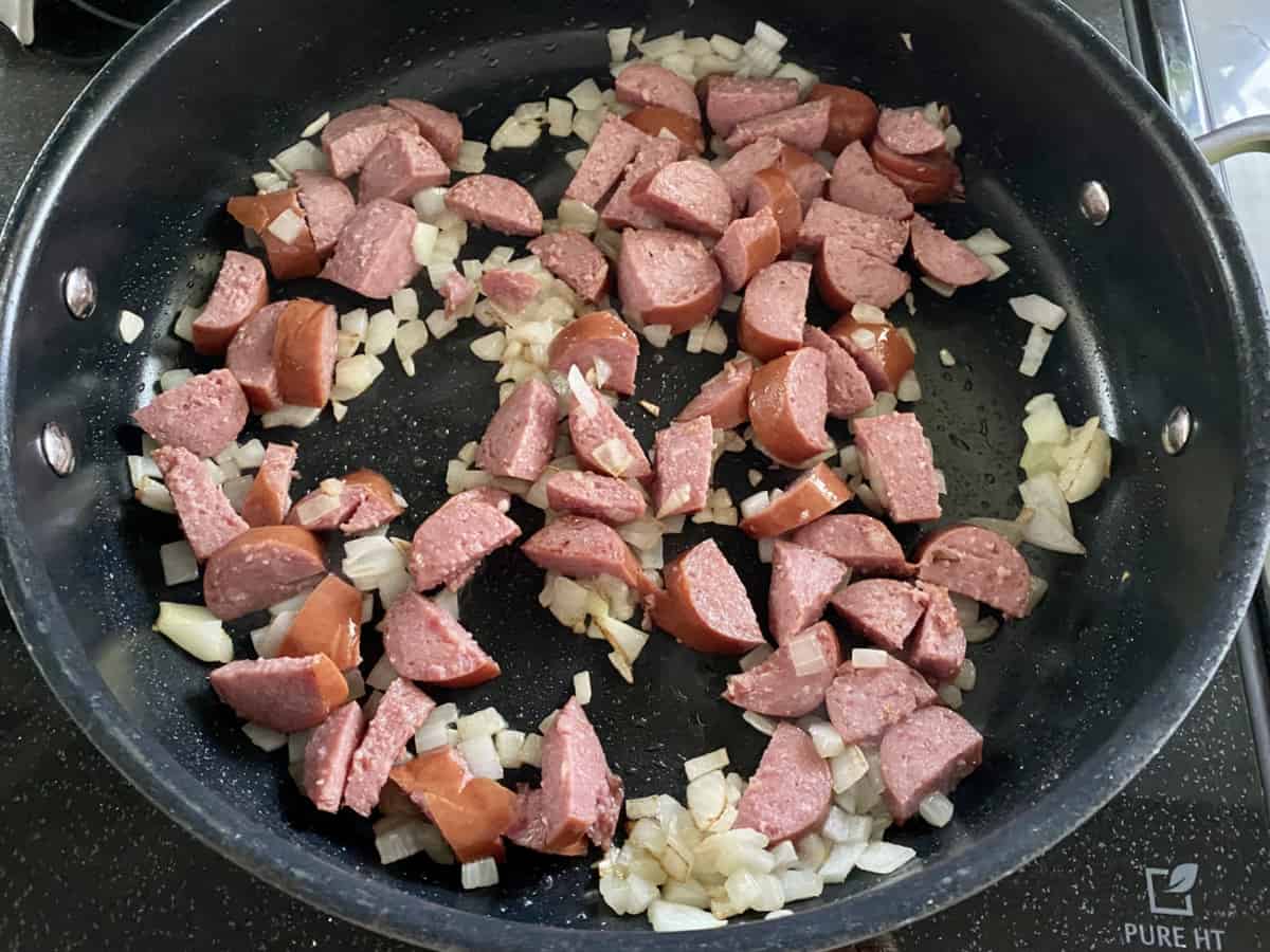 Black skillet with sauteed diced onions and half moon shaped kielbasa peices.