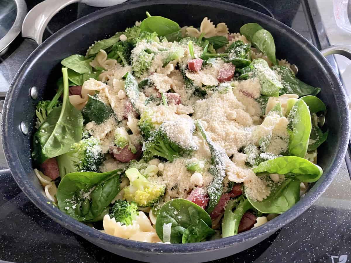 Black skillet filled with spinach, broccoli, and grated pecorino romano cheese.