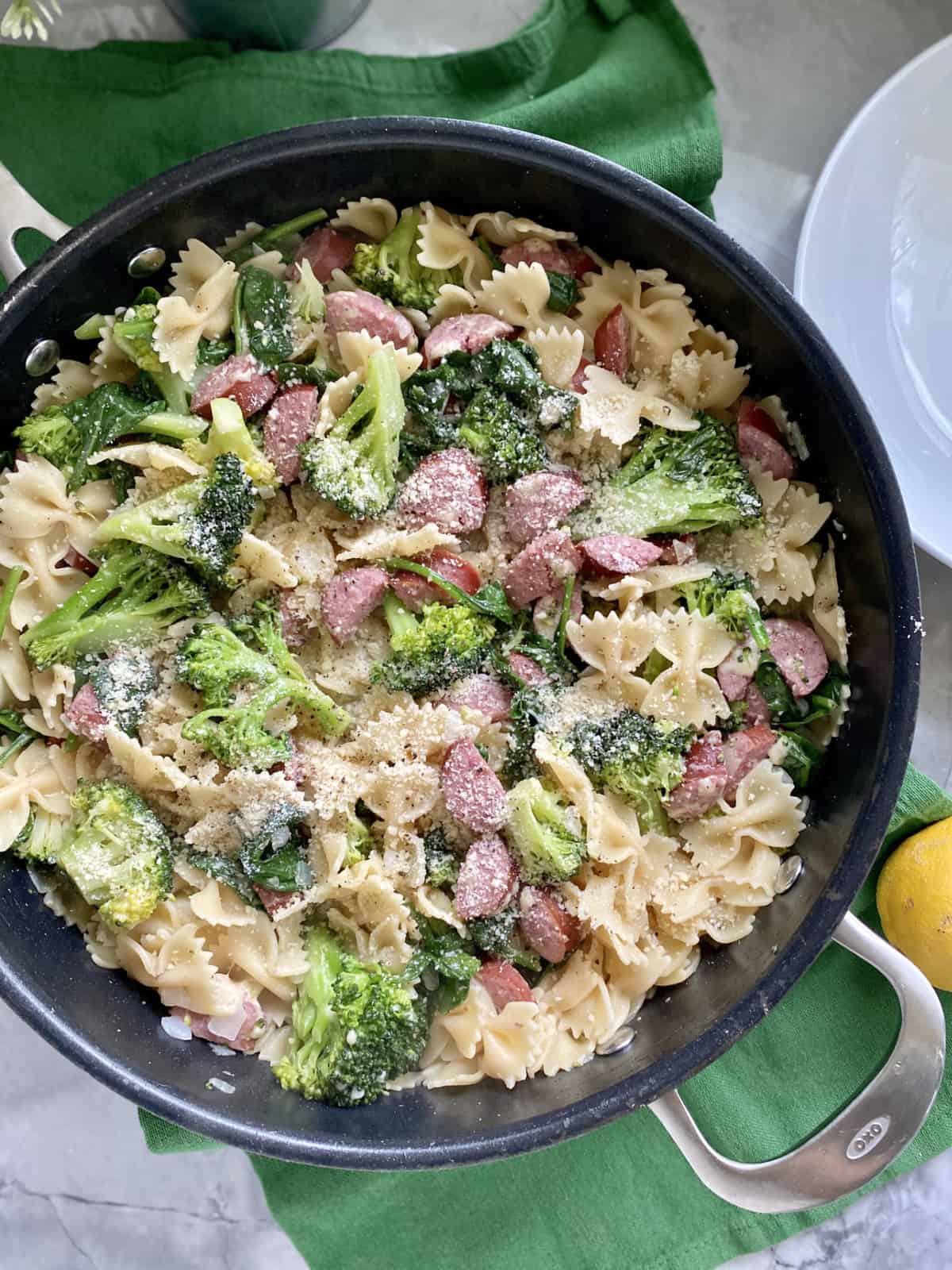 Top view of a black skillet filled with bow tie pasta, broccoli, kielbasa, and cheese.