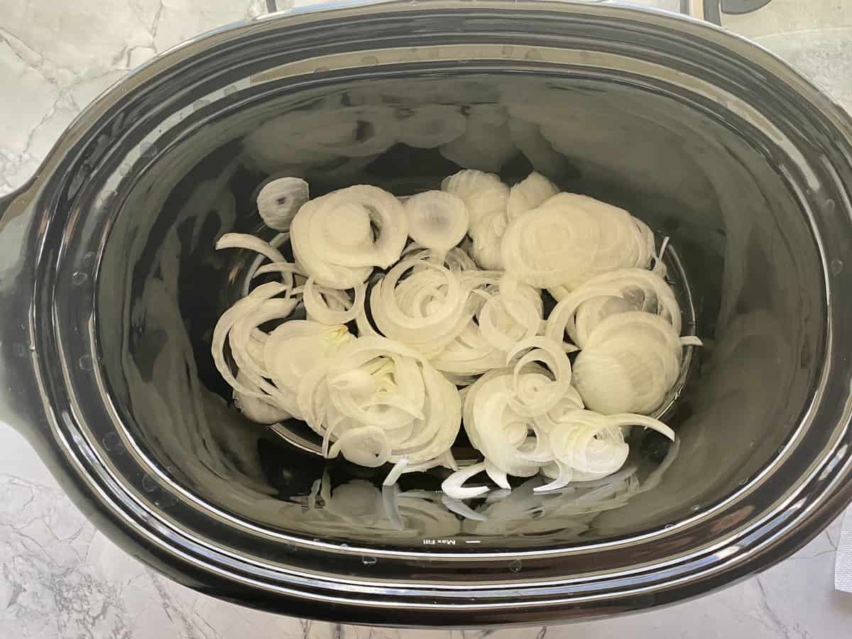 Top view of sliced onions in a black slow cooker.