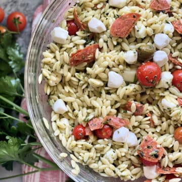 Top view of a glass bowl filled with orzo pasta salad, tomatoes, and mozzarella cheese.