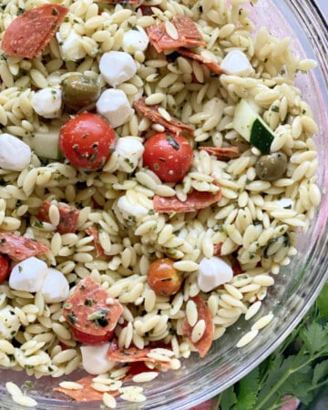 Glass bowl filled with orzo pasta, cheese, tomatoes, and pepperoni.