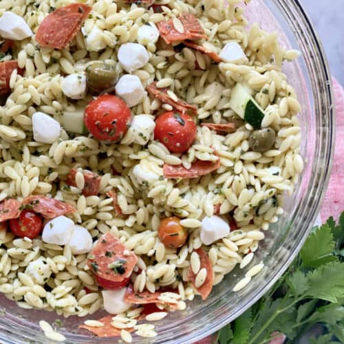 Glass bowl filled with orzo pasta, cheese, tomatoes, and pepperoni.