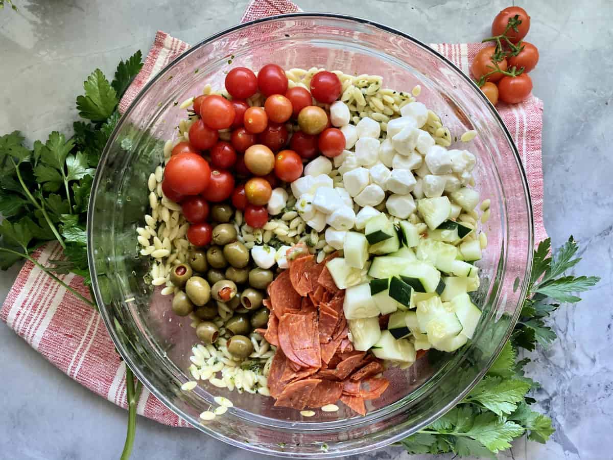 Top view of a glass bowl filled with orzo pasta and veggies on a red and white striped cloth.