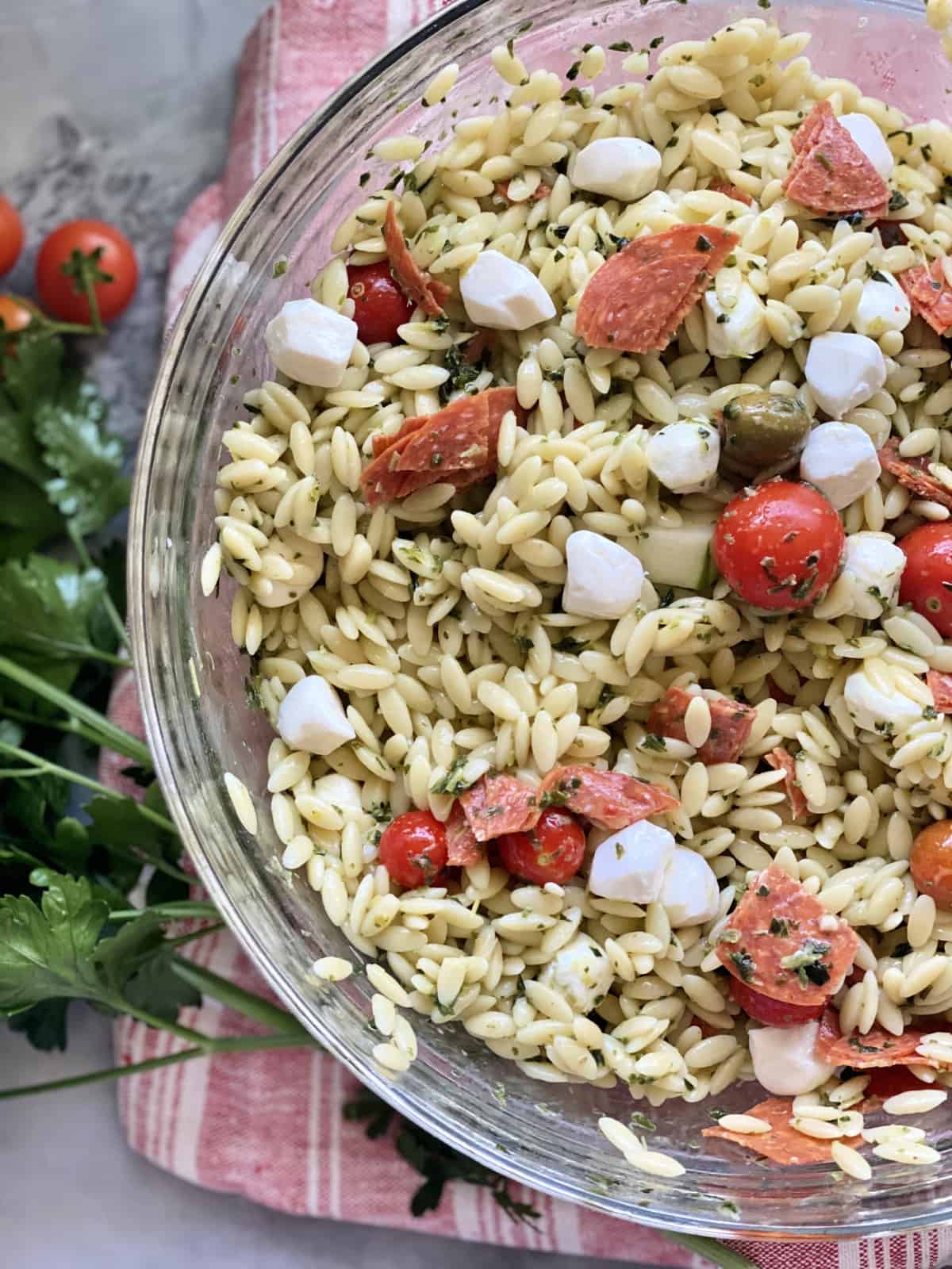 Top view of a glass bowl filled with orzo pasta salad, tomatoes, and mozzarella cheese.