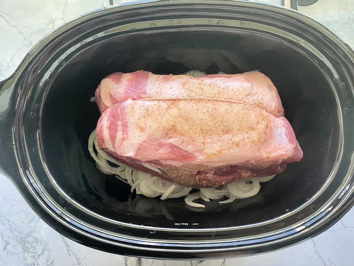 Top view of a raw Boston Butt roast on top of onions in a black slow cooker.