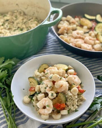 White bowl filled with risotto, shrimp, bay scallops, and zucchini.