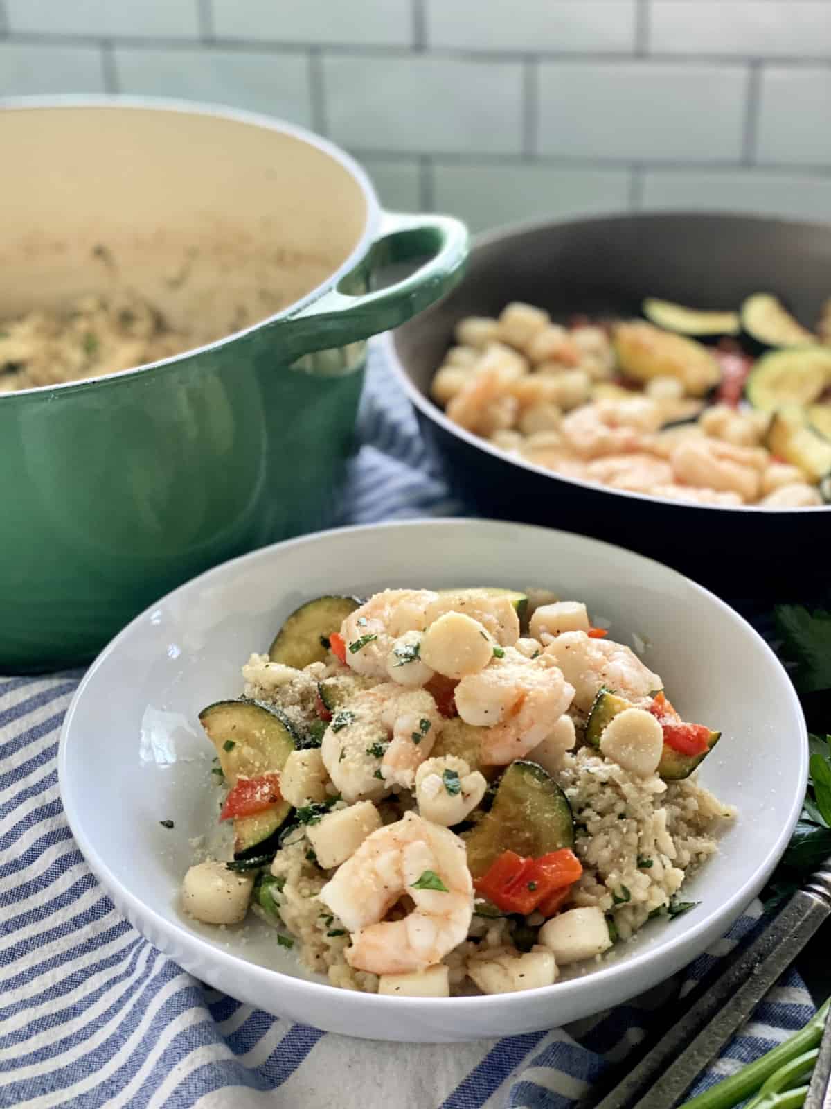 White bowl with seafood risotto with green pot and sauce pan of seafood.