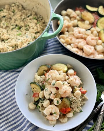 Top view of a white bowl filled with seafood risotto, green pot with risotto, and shrimp in a skillet.