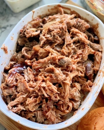 White oval dish with shredded pulled pork and barbecue sauce.