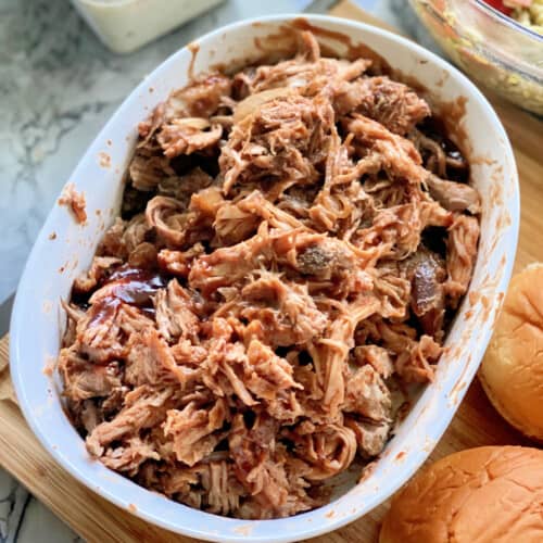 White oval dish with shredded pulled pork and barbecue sauce.