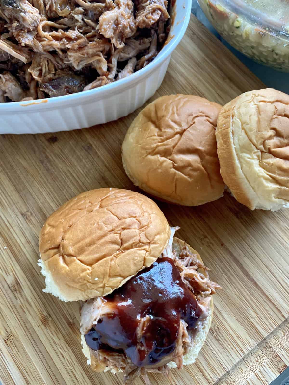 Pulled pork sandwich with barbecue sauce on a wood cutting board.