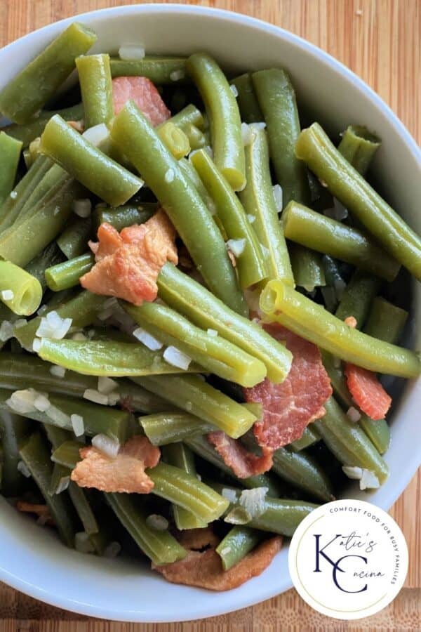 Top view of a white bowl filled with green beans and bacon.