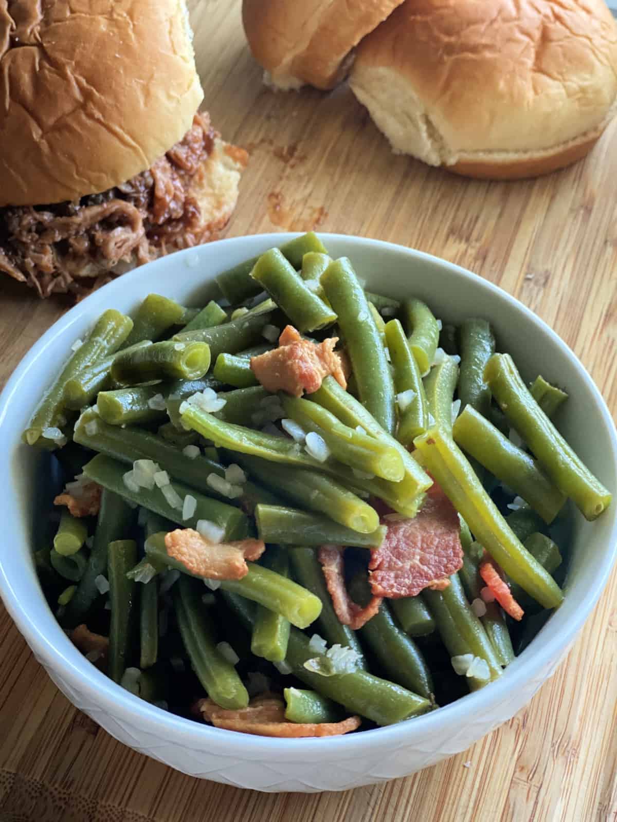 White bowl with chopped green beans, bacon, and onions.