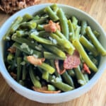 White bowl filled with green beans and bacon on a wood countertop.