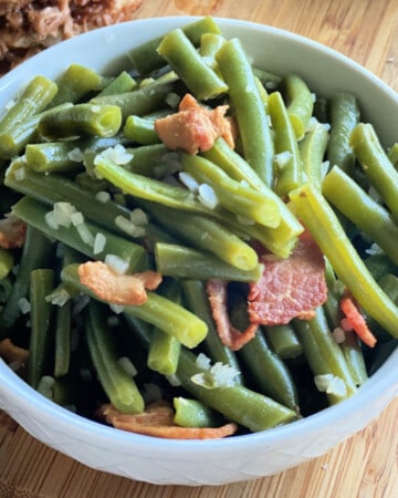 White bowl filled with green beans and bacon on a wood countertop.