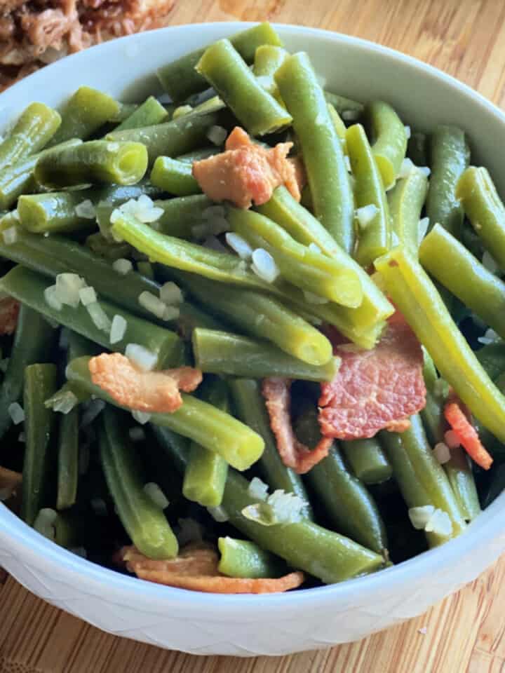 White bowl filled with green beans and bacon on a wood countertop.