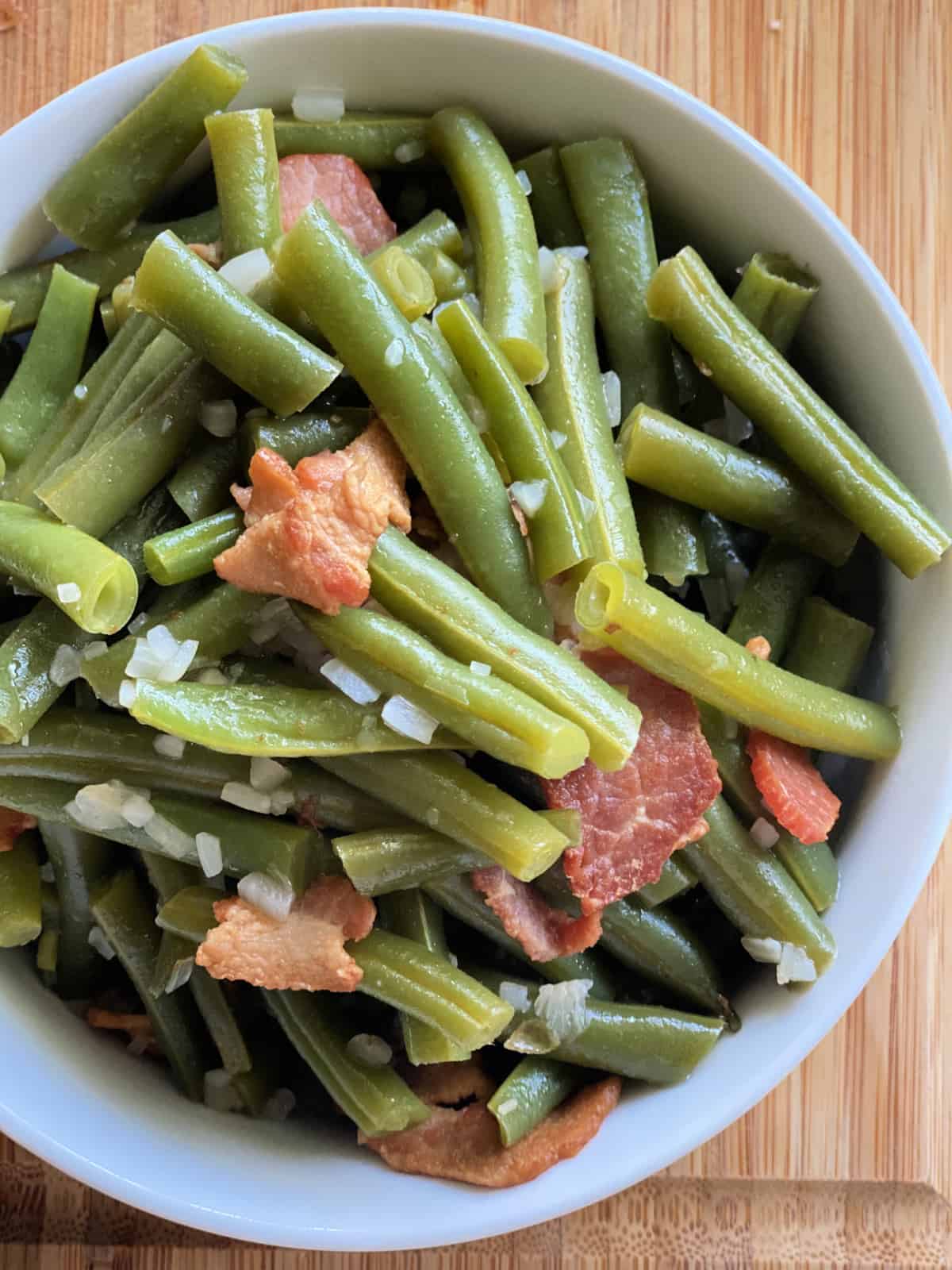 Top view of green beans with bacon and onions on a wood cutting board.