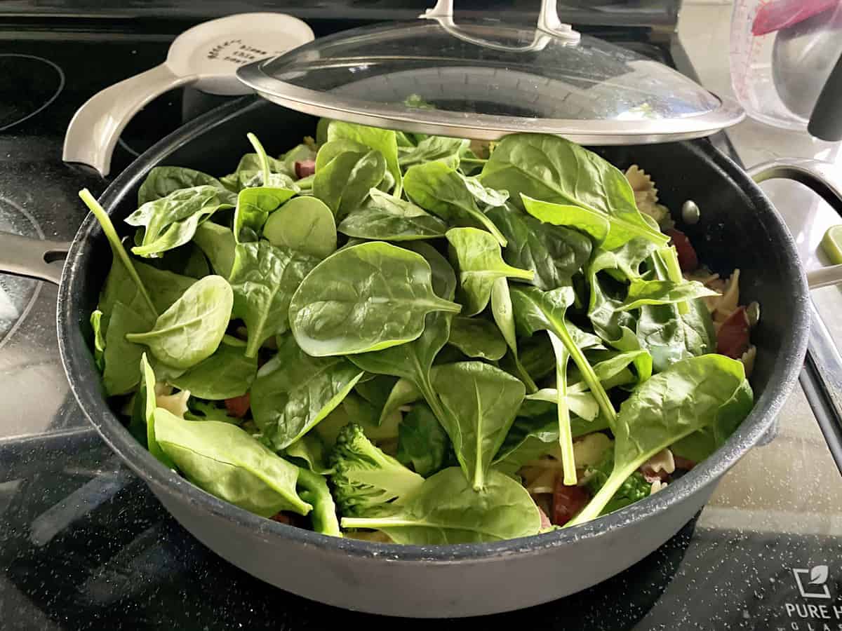 Large skillet filled with spinach with lid on the side.