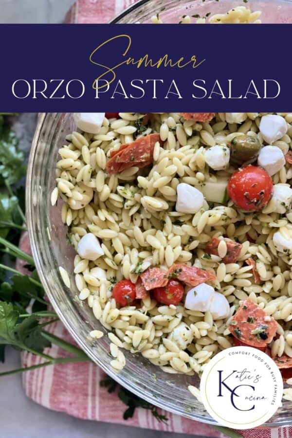 Top view of a glass bowl filled with orzo pasta salad, tomatoes, cucumbers, and mozzarella cheese with text on image for Pinterest.