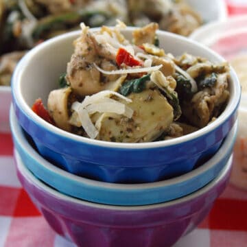 Three bowls stacked with artichoke hearts and tortellinis in it on a red and white checkered table cloth.