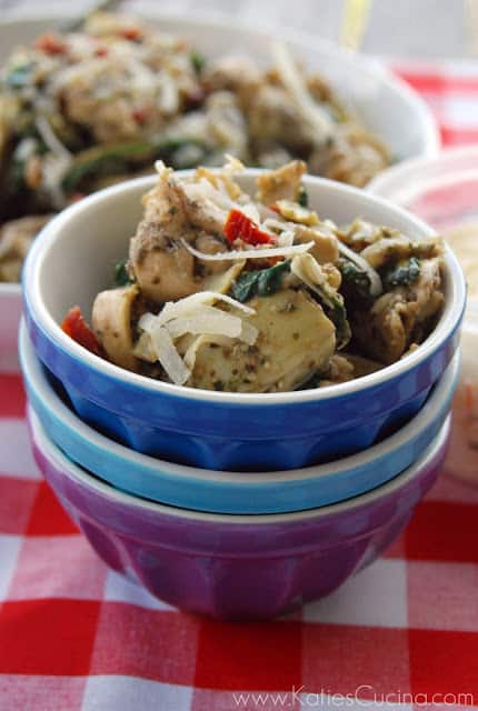 Three bowls stacked with artichoke hearts and tortellinis in it on a red and white checkered table cloth.