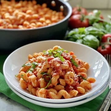 Two white bowls stacked with corkscrew pasta tossed in tomato sauce.