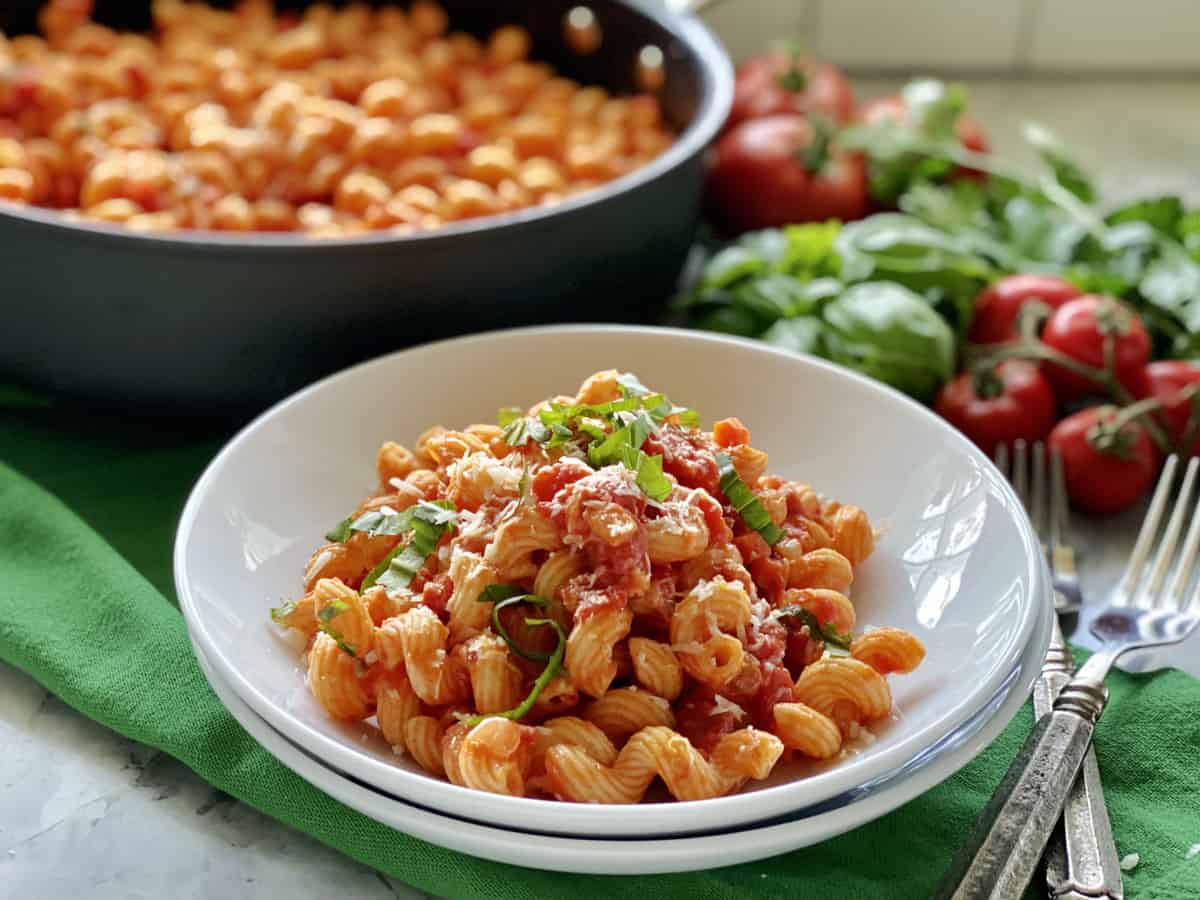 Two white bowls stacked with corkscrew pasta tossed in tomato sauce.